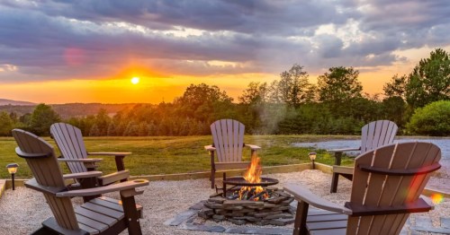 Four Adirondack chairs sit by a fire pit with a beautiful sunset at one of the best cabins in Pennsylvania.