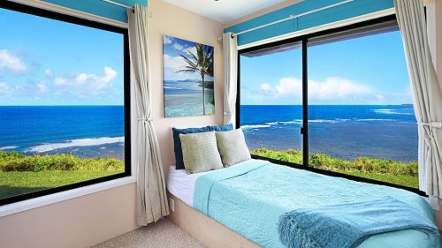 Cozy bedroom with a bed, large windows showcasing a stunning ocean view and blue skies.