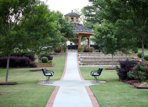 A serene park scene featuring a gazebo, pathway, benches, and lush greenery with flower beds on either side.