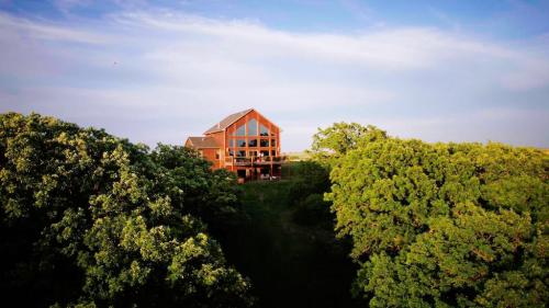 A large wooden house with large windows surrounded by lush green trees under a blue sky.
