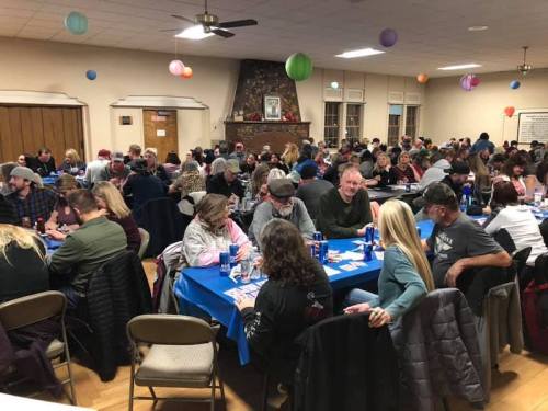A large group of people socializing at tables in a community hall, decorated with colorful paper lanterns.