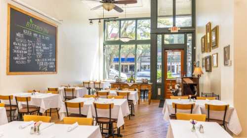 Bright bistro interior with tables set for dining, large windows, and a chalkboard menu on the wall.