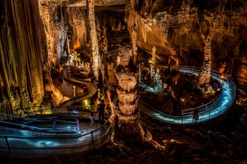 A stunning underground cave with illuminated stalagmites and stalactites, featuring winding pathways and visitors exploring.