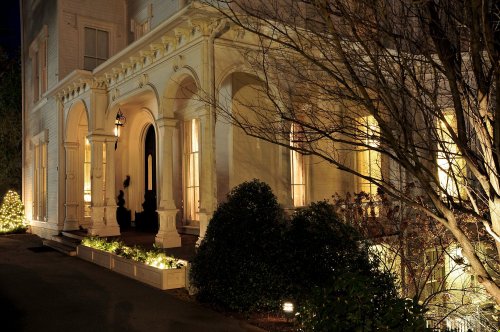 A beautifully lit historic house at night, featuring arched doorways and lush greenery.