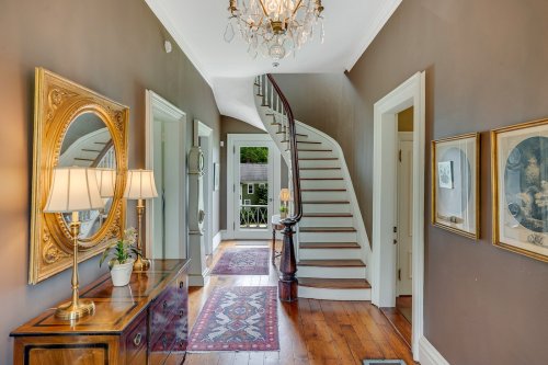 A well-lit hallway featuring a staircase, decorative mirror, lamps, and framed artwork on the walls.