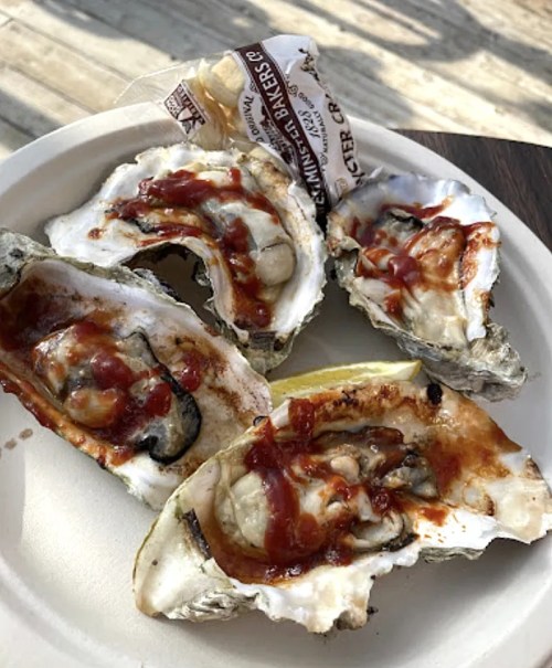 A plate with four oysters topped with sauce and a lemon wedge, served outdoors.