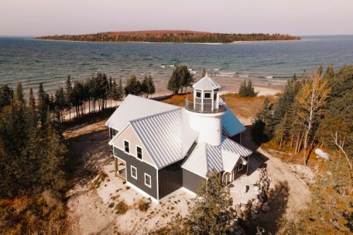 Aerial view of a modern house near a lake, surrounded by trees and with an island visible in the background.