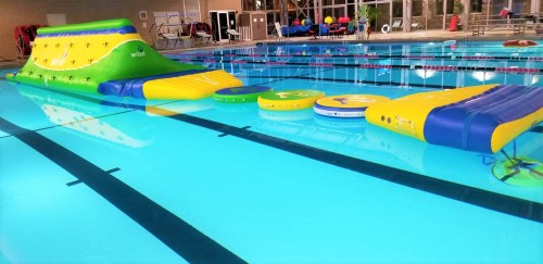 Inflatable water obstacle course in a swimming pool, featuring colorful slides and floating platforms.