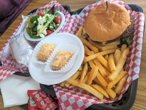 A tray with a burger, fries, a side salad, a baked potato, and two dessert pastries.