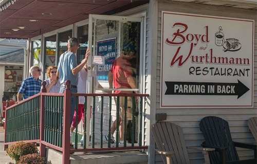A group of people entering Boyd and Wurthmann Restaurant, with a sign indicating parking is in the back.