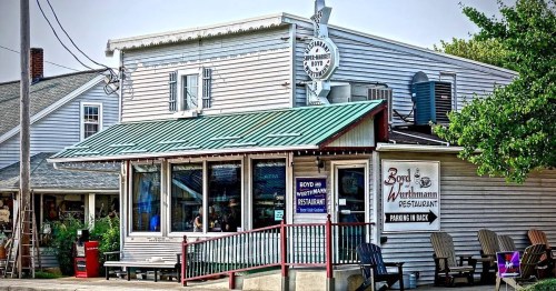 A quaint restaurant with a green awning, featuring a sign and outdoor seating, set in a charming small-town setting.