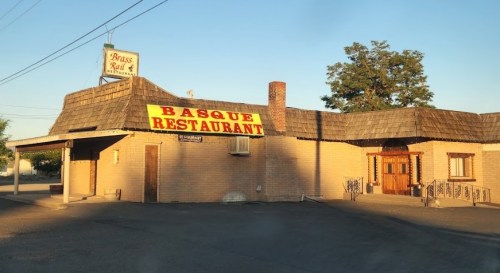 A brick building with a thatched roof and a large sign reading "Basque Restaurant" in a sunny setting.
