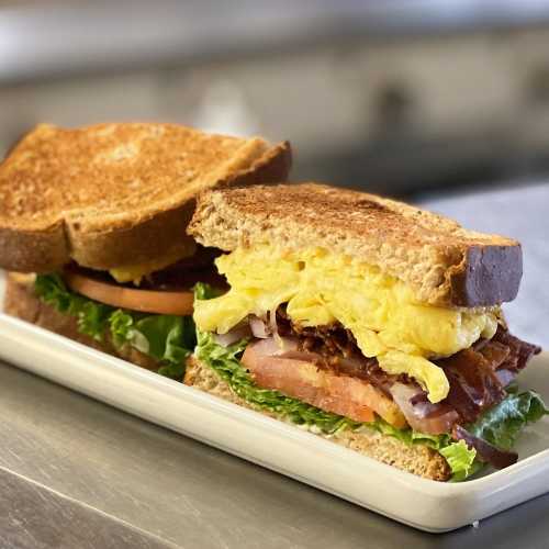 A toasted sandwich filled with lettuce, tomato, bacon, and fluffy scrambled eggs, served on a white plate.