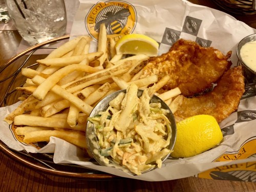 A plate of crispy fried fish with fries, coleslaw, and a lemon wedge, served in a basket.