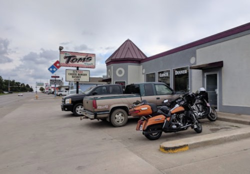 A roadside view of Tom's restaurant with parked cars and motorcycles outside, featuring a sign for Domino's nearby.