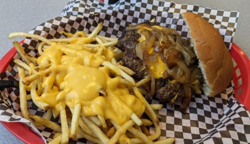 A plate with a cheeseburger topped with onions and a side of cheesy fries on a checkered paper.