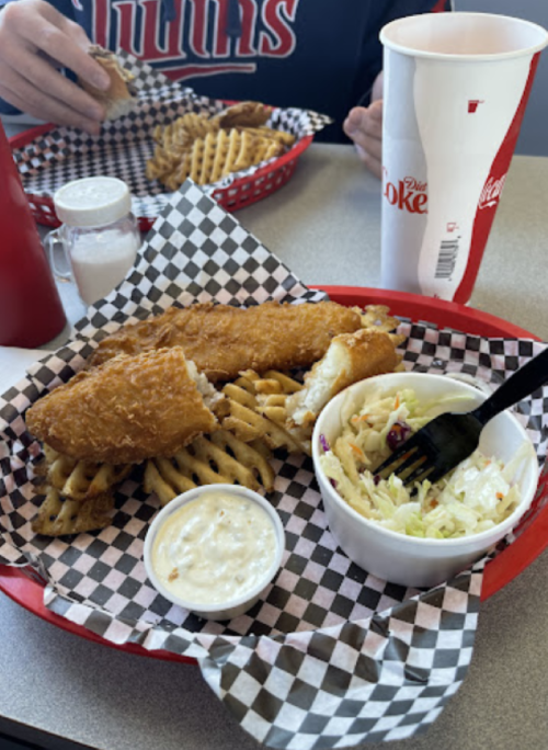 A plate of fried fish with waffle fries, coleslaw, and dipping sauce, served in a red basket on a table.