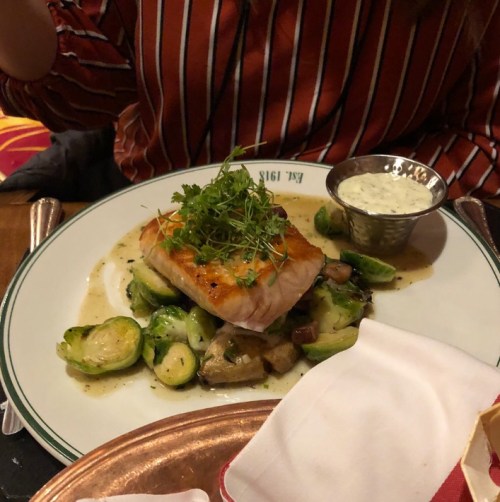 A plate of salmon topped with herbs, served with Brussels sprouts and a side of sauce.