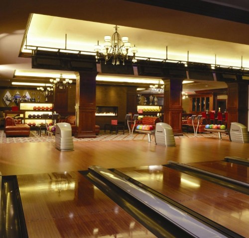 A stylish bowling alley with wooden lanes, elegant lighting, and a cozy lounge area in the background.