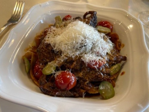 A plate of pasta topped with a rich sauce, cherry tomatoes, green vegetables, and grated cheese.
