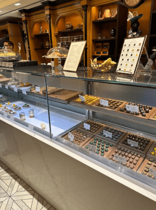 A display case filled with various chocolates and confections, set in a cozy shop with wooden accents.