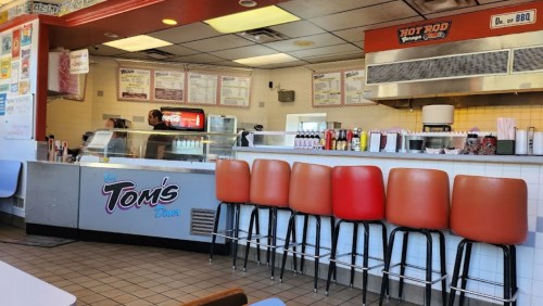 A diner interior with orange stools at the counter, a menu on the wall, and staff preparing food in the background.