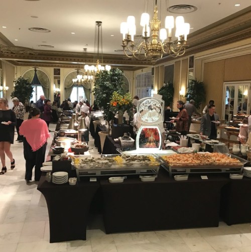 A spacious buffet with various food stations, guests dining, and elegant decor in a well-lit room.