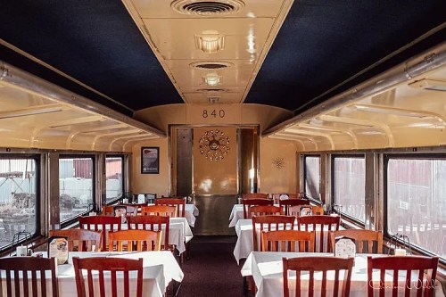 Interior of a vintage train dining car, featuring wooden tables and chairs, with a warm, inviting atmosphere.