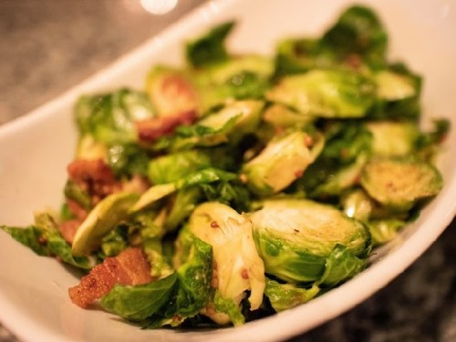 A bowl of sautéed Brussels sprouts with crispy bits, garnished and served on a marble countertop.