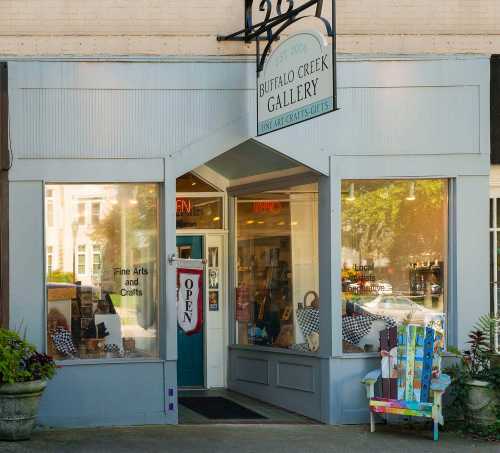 Exterior of Buffalo Creek Gallery, featuring large windows, an "OPEN" sign, and colorful outdoor seating.