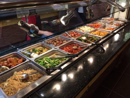 A buffet display featuring various dishes in metal trays, including meats, vegetables, and rice, under warm lights.
