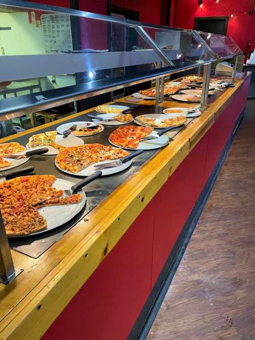 A buffet-style pizza display featuring various types of pizzas on wooden trays under a glass cover.