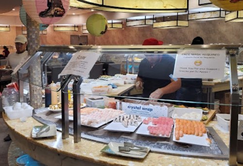 A sushi bar with a variety of sushi and seafood displayed, and a chef preparing food behind a glass counter.