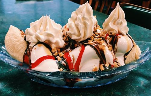 A colorful banana split topped with whipped cream, chocolate syrup, and chopped nuts in a glass dish.