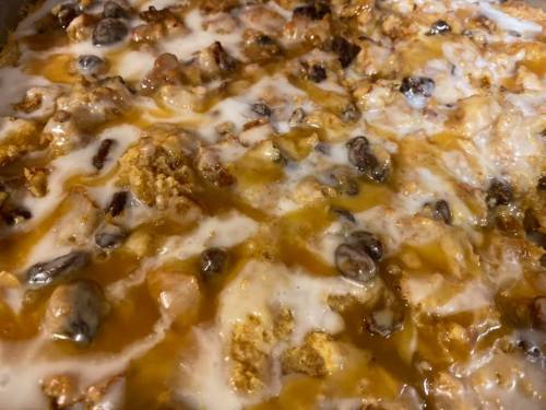 A close-up of a baked dessert with a golden crust, topped with a creamy layer and bits of nuts or fruit.
