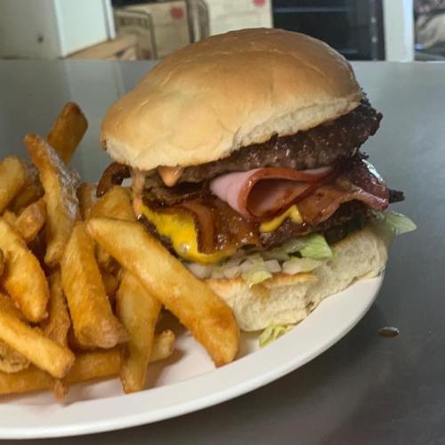 A large burger stacked with beef, bacon, cheese, and toppings, served with a side of golden French fries.