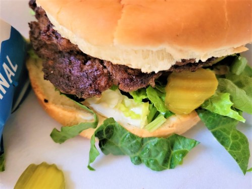 A close-up of a hamburger with a beef patty, lettuce, pickles, and mayonnaise on a soft bun.