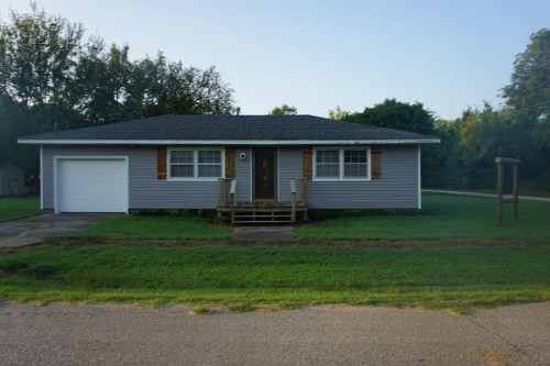 A single-story gray house with a front porch, garage, and green lawn, set on a quiet street.