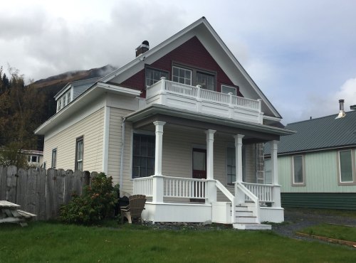 A two-story house with a red and white exterior, featuring a front porch and green grass in the foreground.