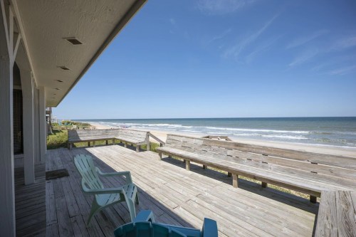 A wooden deck overlooking a sandy beach and calm ocean under a clear blue sky.