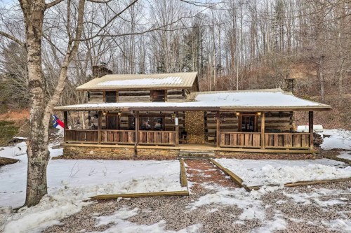 A rustic log cabin with a porch, surrounded by snow and trees, set in a serene winter landscape.