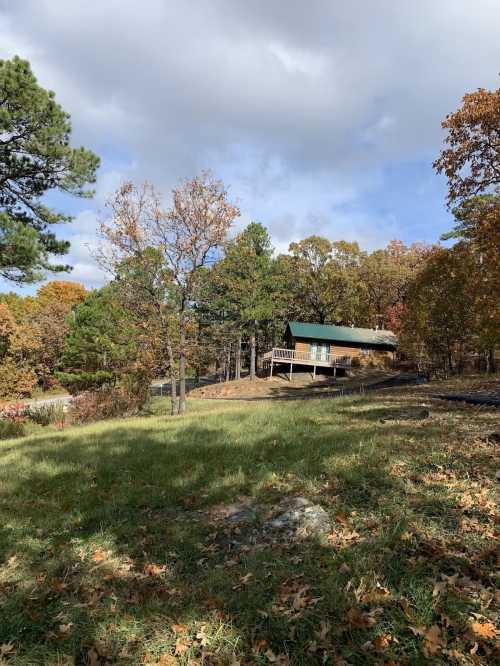 A cozy cabin surrounded by autumn trees and a grassy area under a partly cloudy sky.