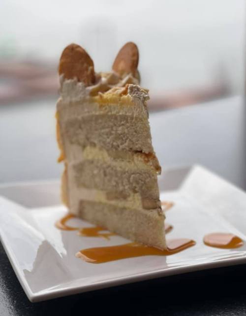 A slice of layered cake on a white plate, drizzled with caramel sauce, with decorative cookie pieces on top.