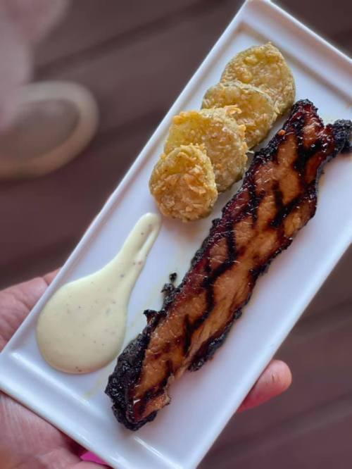 A plate with grilled meat, three fried green tomatoes, and a creamy dipping sauce.