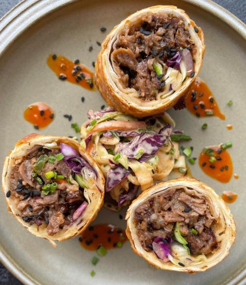 Three crispy rolled wraps filled with beef and vegetables, served on a plate with drizzles of sauce and garnished with herbs.