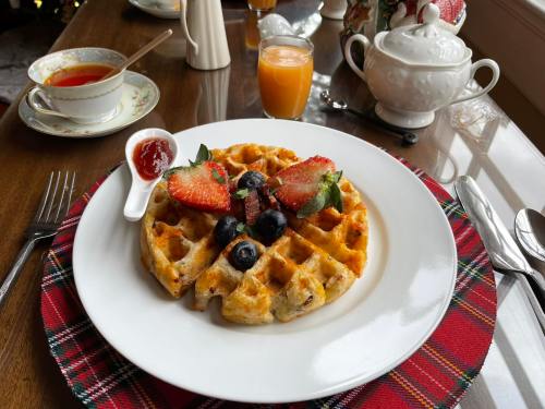 A plate of waffles topped with strawberries and blueberries, served with jam, orange juice, and tea on a tartan placemat.
