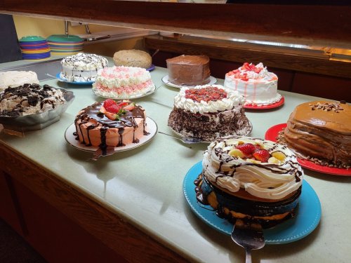 A variety of colorful cakes displayed on a counter, including chocolate, strawberry, and ice cream cakes.