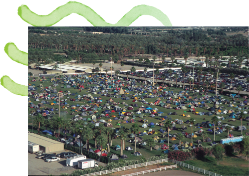 Aerial view of a large campsite with numerous colorful tents set up on a grassy area surrounded by trees.