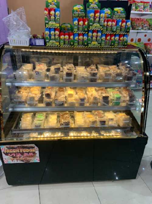 A display case filled with various packaged desserts, including fudge and cakes, in a colorful shop setting.