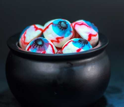 A black cauldron filled with colorful, spooky eyeball treats with blue and red designs.